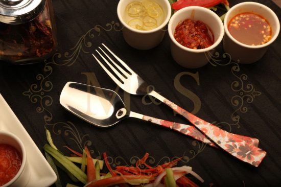 Spoon and fork placed on black cloth with vegetables & sauces beside.